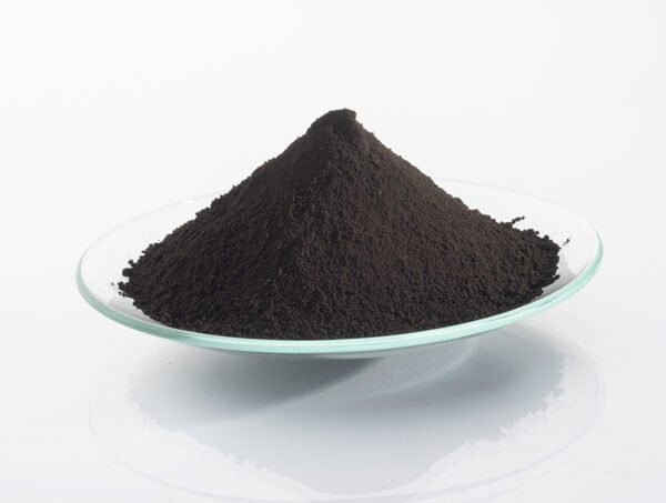 Black iron oxide powder on a clear glass dish for industrial use.