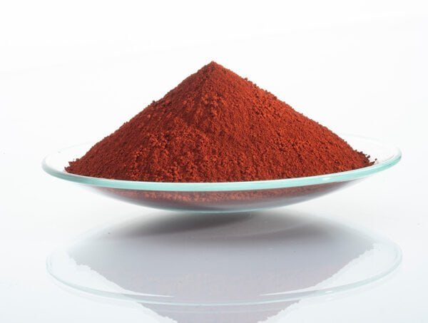 Bright red iron oxide pigment in a glass dish for industrial use.